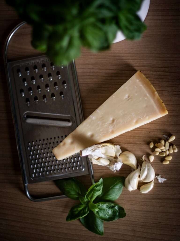 Flat lay of Parmesan cheese, garlic, basil, pine nuts, and grater for homemade pesto.